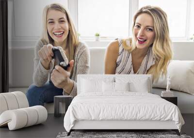 Two Beautiful young woman sitting on sofa with game controller Wall mural