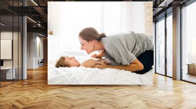 Young mother with her little son relaxing and playing in the bed at the weekend together Wall mural