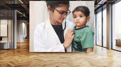 A smiling female doctor holds a baby while showcasing a medicine bottle. Pediatric care concept, promoting child health. Wall mural