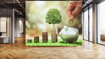 hand putting coins in to piggybank with money stack and plant growing. concept finance and accounting Wall mural