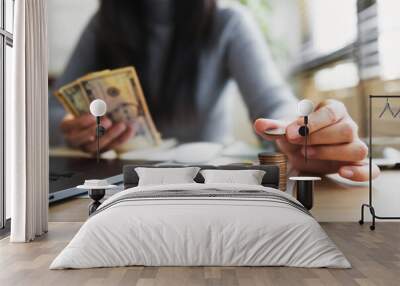 woman is holding a stack of coins and a stack of bills Wall mural