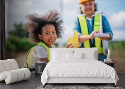 young girl wearing a yellow vest is holding a toy turbine Wall mural