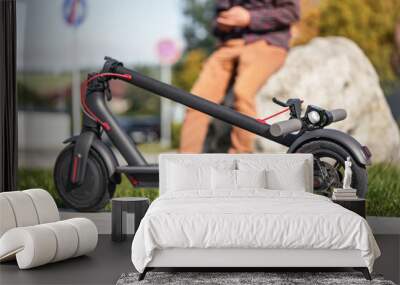 Folded electric scooter on concrete pavement, young man legs in background Wall mural