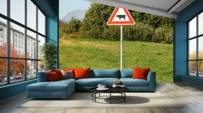 Red triangle warning cows crossing sign, on a green meadow, tree in background. Wall mural