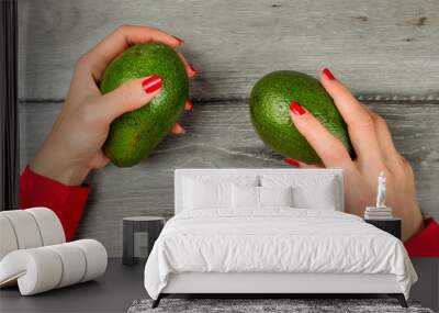 Table top view on woman hands with red nails, holding two green whole avocado over gray wood desk. Wall mural