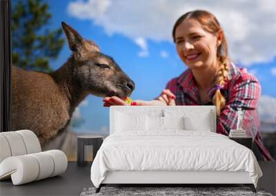 Young woman posing with kangaroo, feeding the animal some fruit from her hand Wall mural