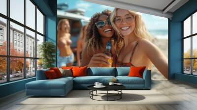 Two women smiling and holding beer at the beach with friends Wall mural