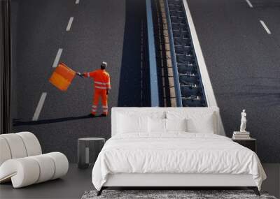 A highway worker with a high visibility work suit waves the orange flag to slow down traffic before the roadblock Wall mural