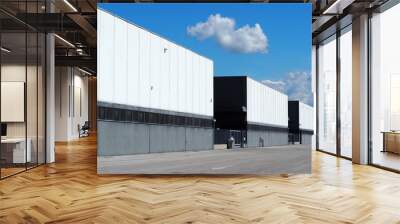 A row of large black and white industrial warehouse buildings  with the road in front . Wall mural