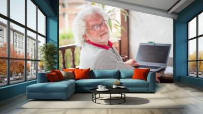 Shallow focus of an old male using a laptop on the table in a garden under the sunlight Wall mural