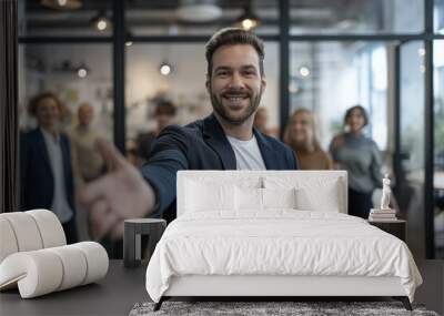 Portrait of businessman welcoming new employee to his business team and company giving hand forward in modern office with colleagues in the background. Wall mural