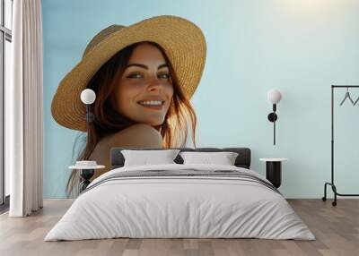 A carefree woman in a light summer outfit and a straw sunhat, looking over her shoulder with a radiant smile under the clear sky Wall mural