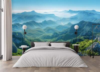 A picturesque mountain range rises majestically under clear blue skies, with green valleys stretching below. The expansive, open areas provide a stunning backdrop with space for overlaying text. Wall mural