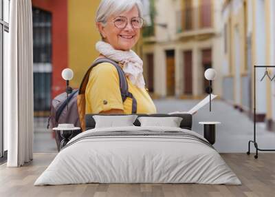 Attractive carefree senior traveler woman carrying backpack visiting the old town of Seville, smiling elderly lady enjoying travel and discovery Wall mural