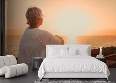 Back view of elderly mature woman sitting alone face the sea at sunset light looking at the horizon. Senior gray-haired woman enjoying freedom and beautiful seascape in vacation Wall mural