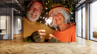 Cheerful caucasian senior couple holding sparklers celebrating new year. Happy lifestyle for mature retirees, party lights Wall mural