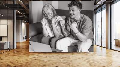 Cheerful couple of boy and elderly grandmother watching summer olympic games together on laptop rejoicing for victory sitting on comfortable sofa in living room Wall mural