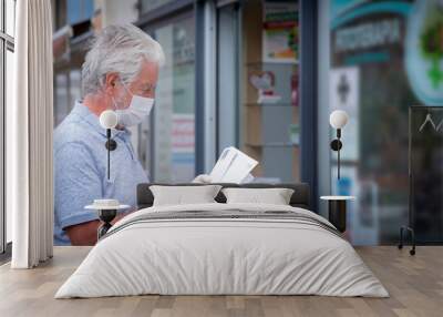 Elderly man with mask and protective gloves leaves the pharmacy with medicines and instructions. Fear of coronavirus infection, covid-19. Concept of retired senior and fear of contagion Wall mural