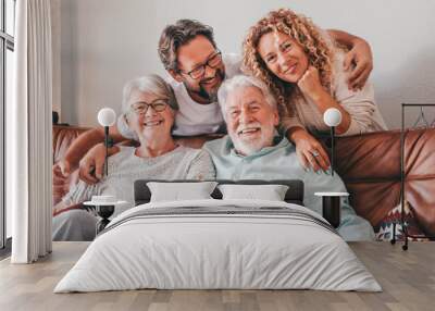 Happy bonding family group relaxing on sofa at home having fun and laughing. Handsome people, parents and adult sons, two generations looking at camera Wall mural