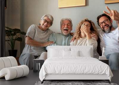 Happy multigenerational family group sitting on sofa at home laughing while spending time together. Beautiful people, parents and adult sons, two generations looking at the camera Wall mural