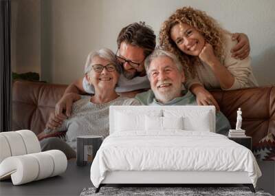 Happy multigenerational family group sitting on sofa at home while spending time together. Four handsome bonding people, two generations looking at the camera Wall mural