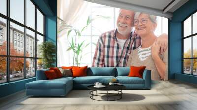 Happy senior couple embracing sitting at home. Modern retirees smiling, expressing happiness and carefree Wall mural