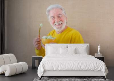 Happy white-haired senior man in yellow shirt isolated on a light background is holding a bowl with cut melon ready to be eaten Wall mural