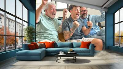 Males from multigenerational family sitting together at home looking at tv enthusiastically cheer athletes of Olympic games. Sports and participation of three attractive men of different ages Wall mural