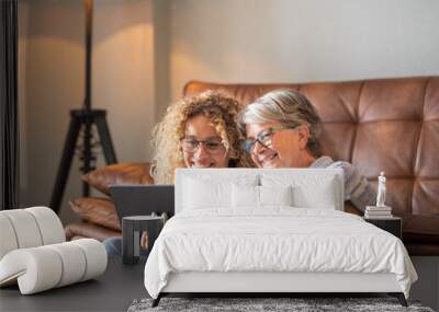 Mother with adult daughter at home having fun together sharing social media on digital tablet Wall mural