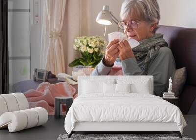 Older adult caucasian woman with severe cold and fever symptoms such as seasonal flu or pollen allergy - woman on sofa at home with blanket Wall mural