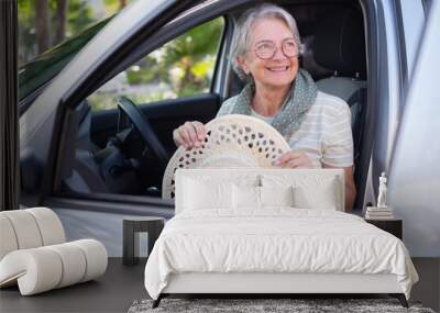 Portrait of attractive smiling senior woman casual dressed entering the car holding her hat Wall mural