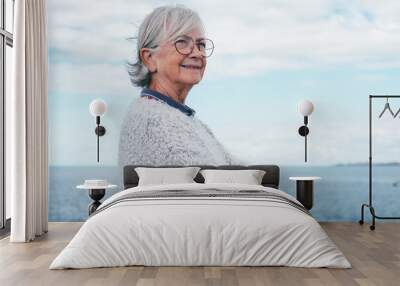 Portrait of pensive handsome senior woman standing by the sea looking away. Smiling elderly white-haired lady in outdoor excursion enjoying freedom, relax and retirement Wall mural