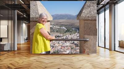 Portrait of smiling senior woman visiting a historic castle in Andalusia, Spain, looking at landscape from the top. Travel and tourism concept, adventure is ageless Wall mural