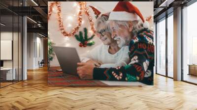 Senior couple in Christmas sweeter and santa hat using laptop computer together. Elderly happy couple celebrate Christmas event with decorated desk and wall. Merry Christmas and happy new year Wall mural