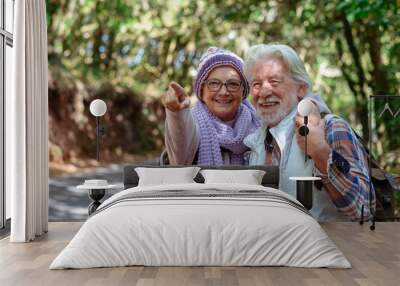 Senior couple together in a forest setting smiling enjoying nature and healthy lifestyle. Two retired man and woman embrace looking around symbolizing their close bond and happiness Wall mural