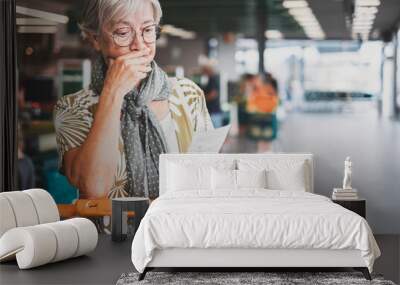 Senior woman in the supermarket checks her grocery receipt looking worried about rising costs - elderly lady pushing shopping cart, consumerism concept, rising prices, inflation Wall mural