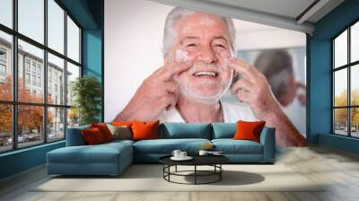 Skin care. Handsome elderly bearded man in bathrobe applying cream on his face as a daily routine Wall mural