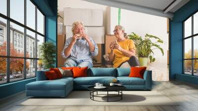 Smiling couple of senior people white hair working in the new empty apartment with moving boxes, sitting on the floor having break - concept of active elderly people and new beginning like retired Wall mural