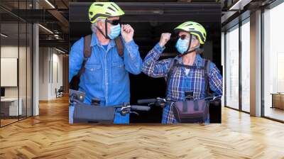 Two senior people with bicycle, an elderly man and woman, greet each other by touching their elbows instead of hugging or shaking hands. Wall mural