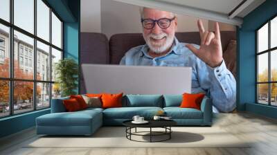 Video call concept. .Handsome smiling bearded senior man gesturing positivity with hand talking on computer using laptop webcam to communicate in video chat Wall mural