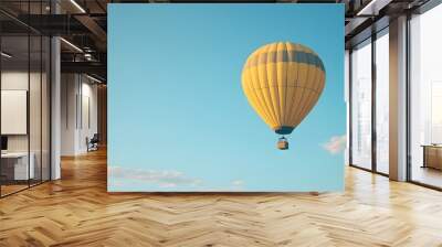 A hot air balloon flying in the sky, with a yellow and black checkered pattern. Against a clear blue background with copy space Wall mural