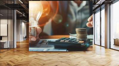 business man hand holding lightbulb with using calculator to calculate and money stack. idea saving energy and accounting finance in office concept Wall mural