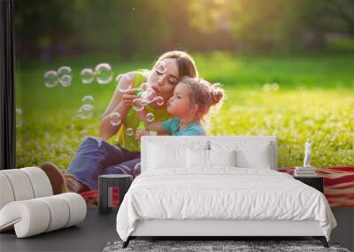 Family in park -Female child blows soup foam and make bubbles with her mother in nature. Wall mural