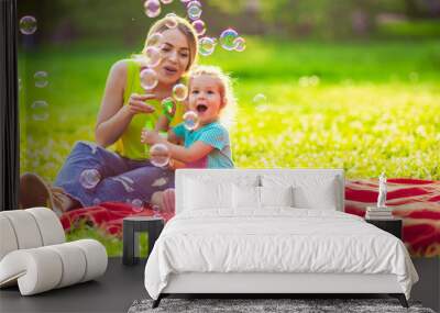 Happy family in park -Female child blows soup foam and make bubbles with her mother in nature. Wall mural