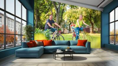 Happy family. Smiling father and mother with kid on bicycles having fun in park.. Wall mural