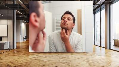 Morning hygiene, man in the bathroom looking in mirror and and checks his beard. Wall mural