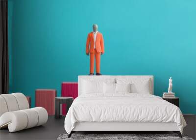 A miniature figurine in an orange suit standing atop pink bar graph columns, symbolizing success and achievement in business. Wall mural