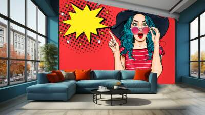 Pop Art Woman surprised in hat and glasses showing product .Beautiful girl with curly hair pointing to on bubble . Presenting your product. Expressive facial expressions Wall mural