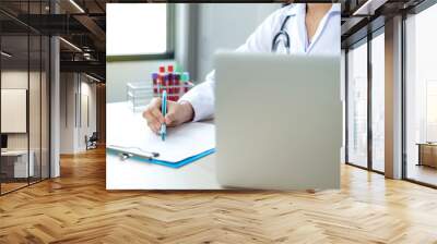 The doctor records the health examination results and medication usage of the patient on the chart and laptop, medical check up concept. Wall mural