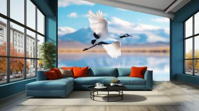 A majestic crane gracefully soars over a tranquil lake, reflecting stunning blue skies and distant mountains. Wall mural